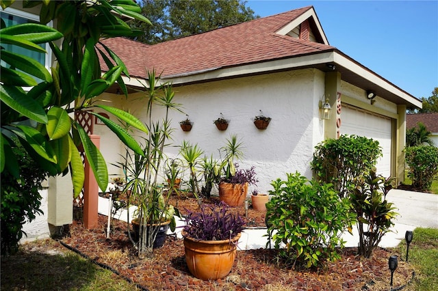 view of side of home with an attached garage, a shingled roof, concrete driveway, and stucco siding