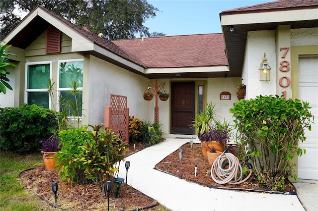 entrance to property featuring a garage, roof with shingles, and stucco siding