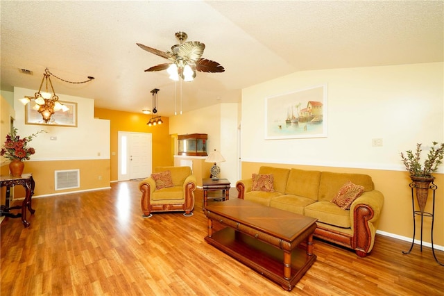 living room with a textured ceiling, light hardwood / wood-style floors, ceiling fan with notable chandelier, and vaulted ceiling