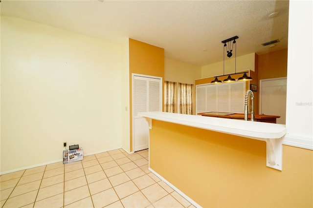 kitchen with light tile patterned floors, visible vents, hanging light fixtures, a textured ceiling, and a kitchen bar