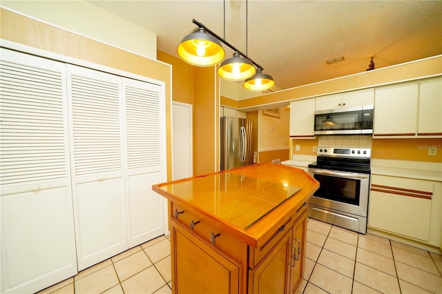 kitchen featuring appliances with stainless steel finishes, tasteful backsplash, a textured ceiling, light tile patterned flooring, and hanging light fixtures