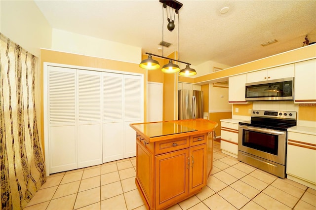 kitchen featuring light tile patterned floors, a textured ceiling, stainless steel appliances, a kitchen island, and light countertops