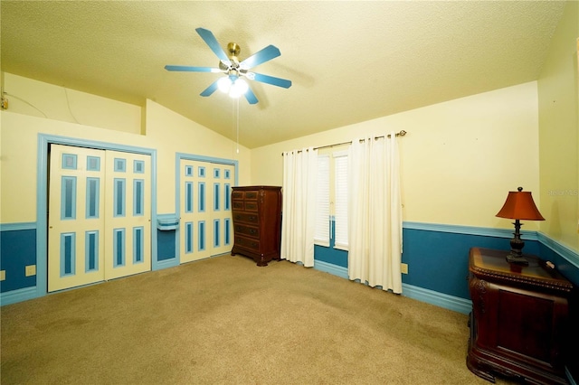 interior space featuring a textured ceiling, carpet flooring, vaulted ceiling, and ceiling fan