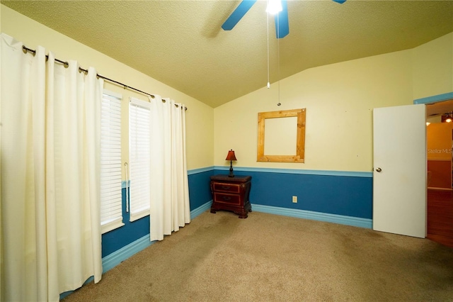 spare room featuring carpet, a ceiling fan, vaulted ceiling, a textured ceiling, and baseboards