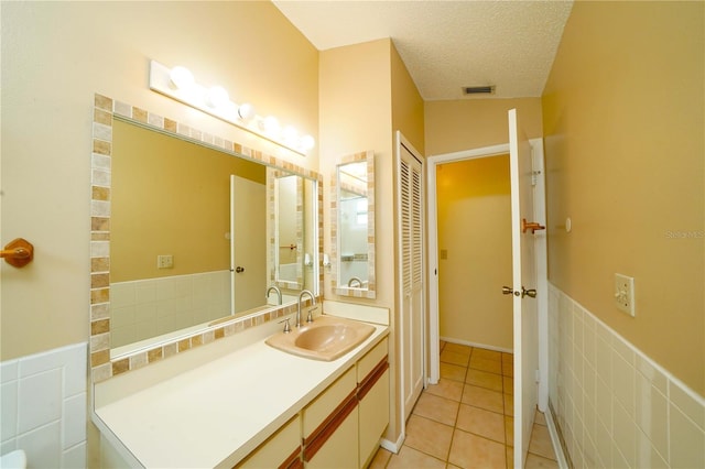 bathroom featuring backsplash, tile patterned flooring, vanity, tile walls, and a textured ceiling