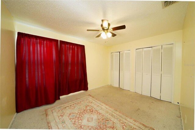 bedroom with ceiling fan, multiple closets, light colored carpet, and a textured ceiling