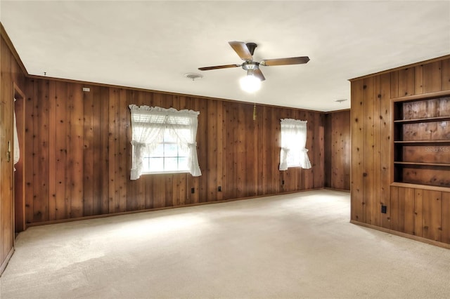 unfurnished room with wood walls, ceiling fan, and light colored carpet