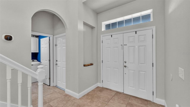 entryway with arched walkways, light tile patterned flooring, washer / dryer, and baseboards