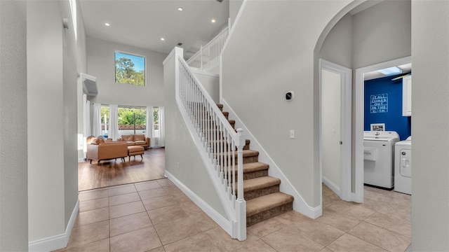 staircase with tile patterned floors, a high ceiling, arched walkways, baseboards, and washing machine and dryer