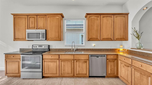 kitchen with stainless steel appliances, a sink, dark countertops, brown cabinetry, and recessed lighting