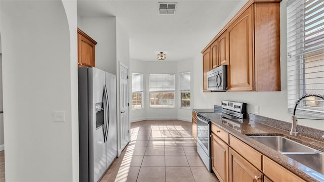 kitchen featuring stainless steel appliances, a sink, dark stone counters, baseboards, and light tile patterned floors