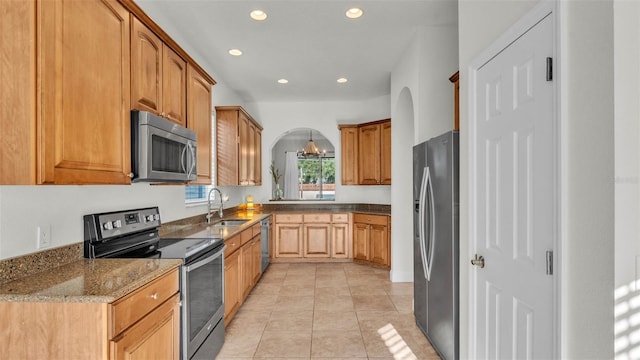 kitchen featuring stainless steel appliances, a sink, recessed lighting, arched walkways, and stone countertops