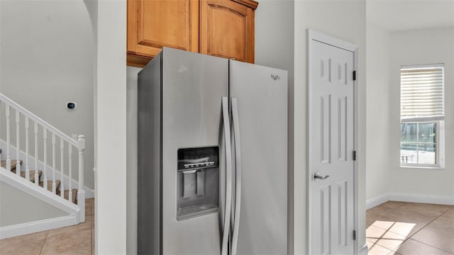 kitchen featuring stainless steel refrigerator with ice dispenser, light tile patterned floors, baseboards, and brown cabinetry