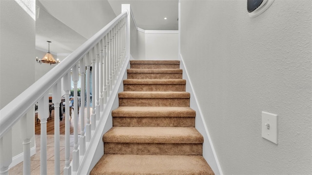 stairs featuring a chandelier, ornamental molding, a textured wall, and carpet floors