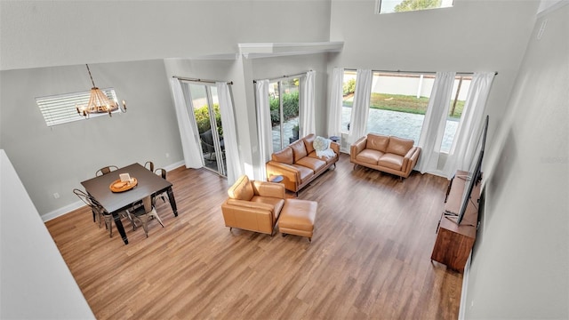 living area with a chandelier, a towering ceiling, wood finished floors, and baseboards