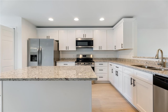 kitchen with a center island, sink, light wood-type flooring, appliances with stainless steel finishes, and white cabinetry