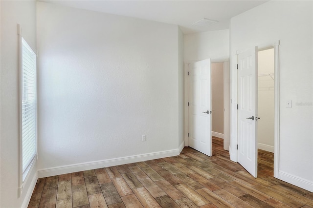 unfurnished bedroom with a walk in closet, a closet, multiple windows, and hardwood / wood-style flooring