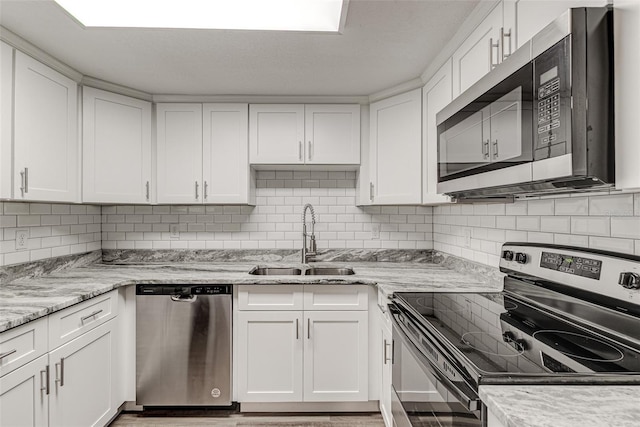 kitchen with light stone counters, backsplash, appliances with stainless steel finishes, white cabinetry, and a sink