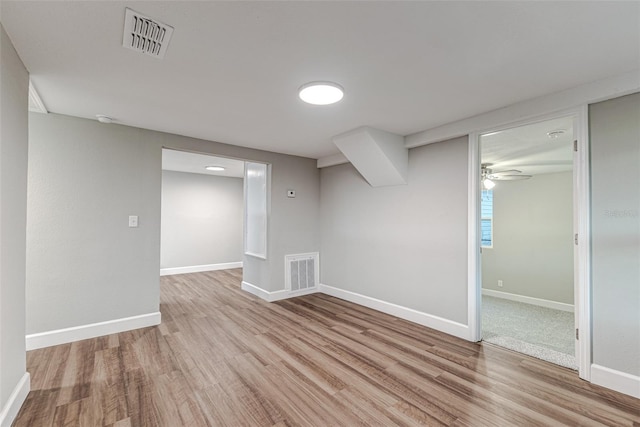 basement featuring light wood-style floors, baseboards, visible vents, and a ceiling fan