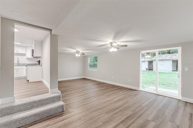 unfurnished living room featuring a ceiling fan, light wood-type flooring, a sink, and baseboards