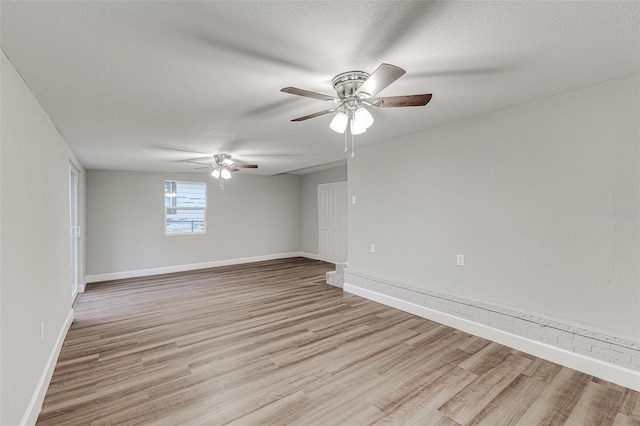 spare room with light wood-style flooring, baseboards, ceiling fan, and a textured ceiling