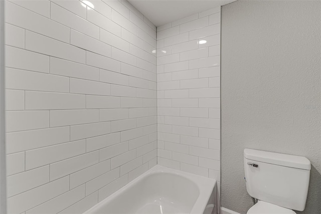 bathroom with a textured wall, bathtub / shower combination, and toilet