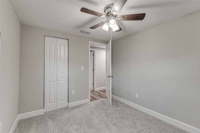 unfurnished bedroom with a closet, light colored carpet, visible vents, a textured ceiling, and baseboards