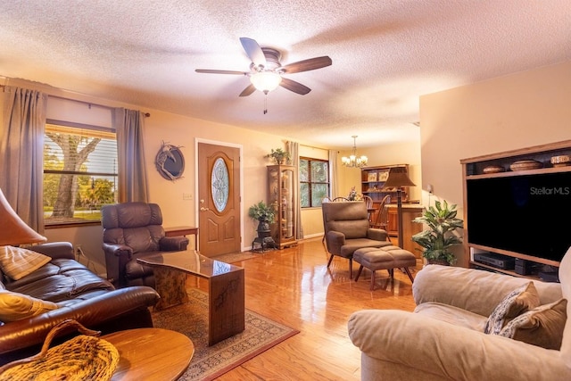 living room featuring ceiling fan with notable chandelier, light hardwood / wood-style floors, and a textured ceiling