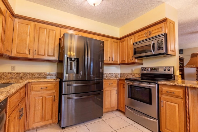 kitchen with light tile patterned floors, appliances with stainless steel finishes, light stone counters, and a textured ceiling