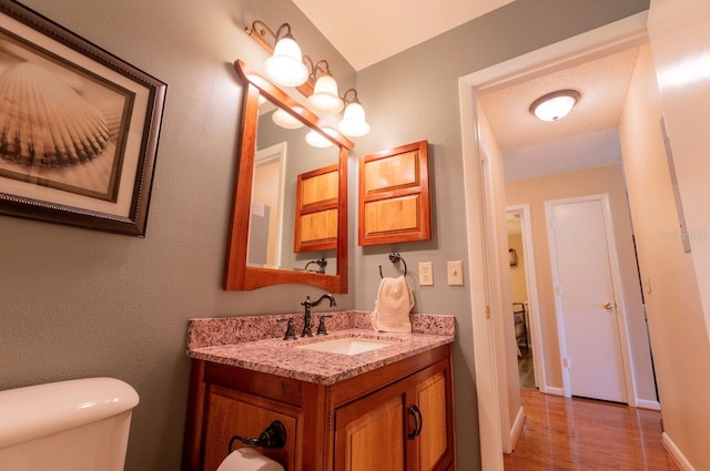 bathroom featuring wood-type flooring, toilet, a textured ceiling, and vanity