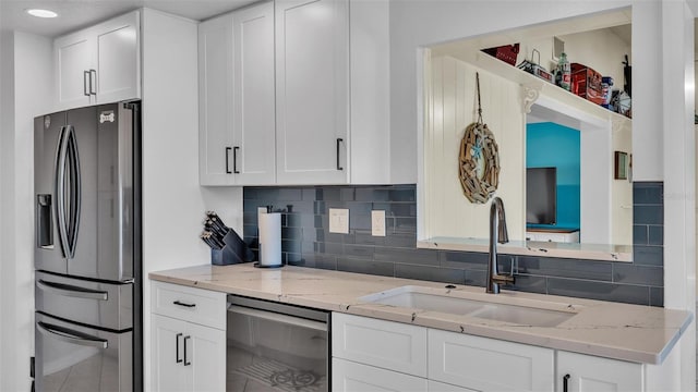 kitchen featuring stainless steel fridge, light stone countertops, dishwasher, sink, and white cabinetry