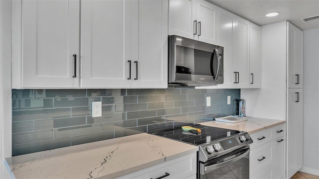 kitchen featuring appliances with stainless steel finishes, white cabinetry, light stone counters, and tasteful backsplash