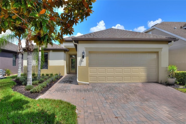 ranch-style house with a shingled roof, decorative driveway, an attached garage, and stucco siding