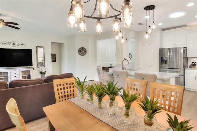 dining area featuring ceiling fan with notable chandelier, light wood-type flooring, and sink