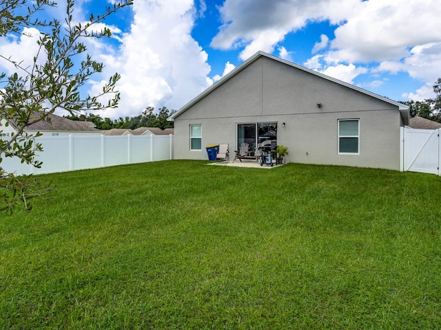 rear view of property featuring a yard, stucco siding, a gate, a patio area, and a fenced backyard