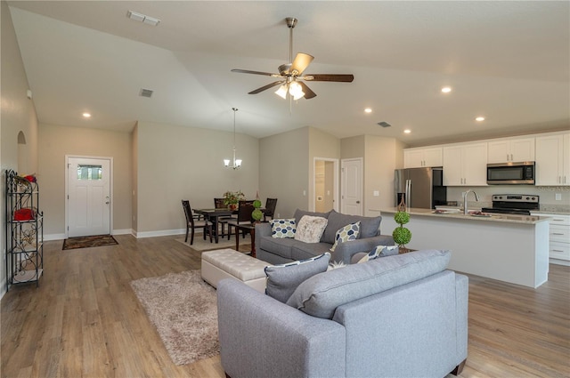 living room featuring sink, ceiling fan with notable chandelier, light hardwood / wood-style flooring, and vaulted ceiling