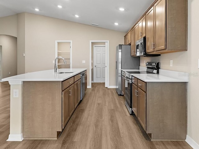 kitchen featuring sink, an island with sink, vaulted ceiling, appliances with stainless steel finishes, and light wood-type flooring