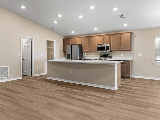 kitchen with an island with sink, light hardwood / wood-style floors, lofted ceiling, and appliances with stainless steel finishes