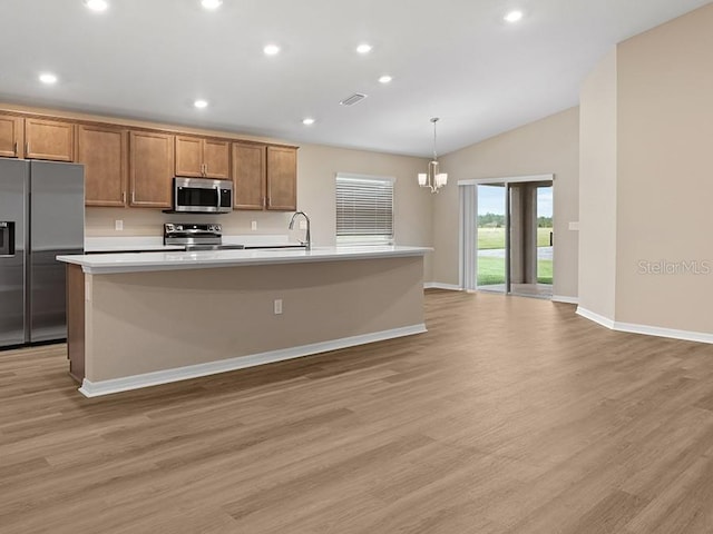 kitchen with appliances with stainless steel finishes, light wood-type flooring, a kitchen island with sink, pendant lighting, and lofted ceiling