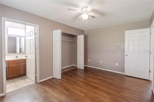 unfurnished bedroom featuring a textured ceiling, a closet, connected bathroom, ceiling fan, and light wood-type flooring