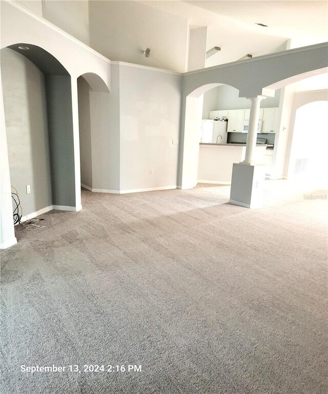 unfurnished living room with light carpet, crown molding, and a towering ceiling