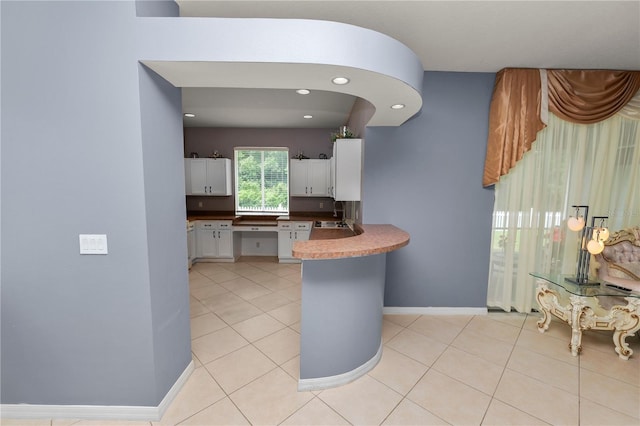 kitchen featuring white cabinets, light tile patterned floors, kitchen peninsula, and sink