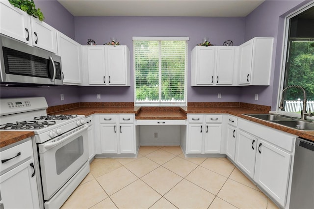 kitchen with sink, light tile patterned floors, appliances with stainless steel finishes, and white cabinets