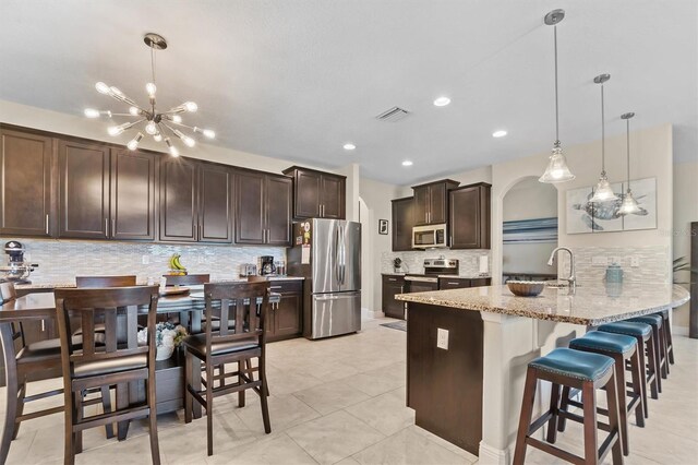 kitchen with stainless steel appliances, visible vents, hanging light fixtures, and light stone countertops