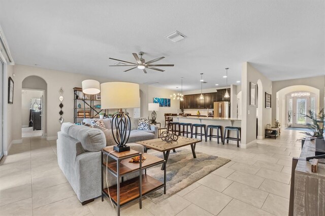 living room with ceiling fan with notable chandelier, arched walkways, visible vents, and light tile patterned flooring