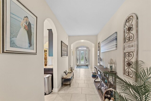 hallway with arched walkways, baseboards, and light tile patterned floors