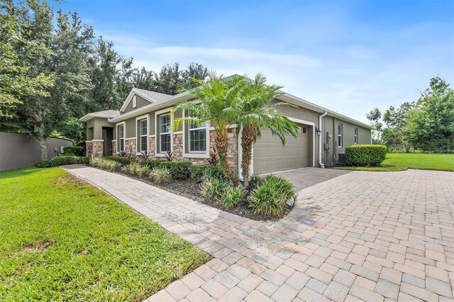 view of front of house with decorative driveway, stucco siding, a front yard, a garage, and stone siding