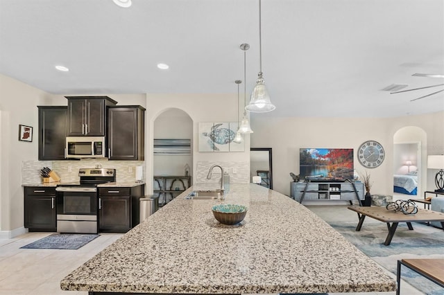 kitchen with arched walkways, appliances with stainless steel finishes, a sink, and pendant lighting