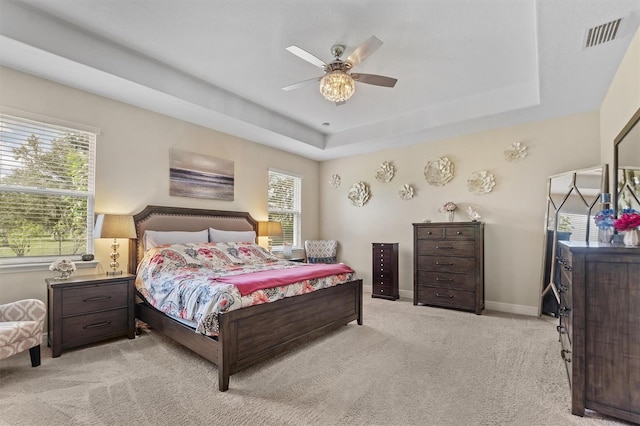 bedroom with light colored carpet, a raised ceiling, visible vents, and baseboards