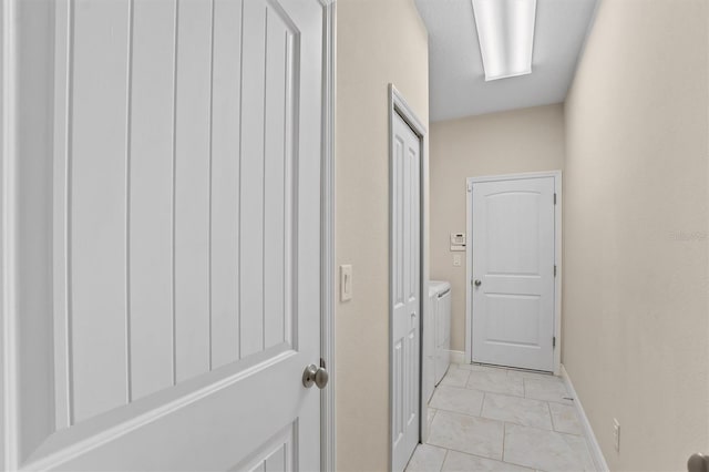 corridor featuring light tile patterned flooring, independent washer and dryer, and baseboards